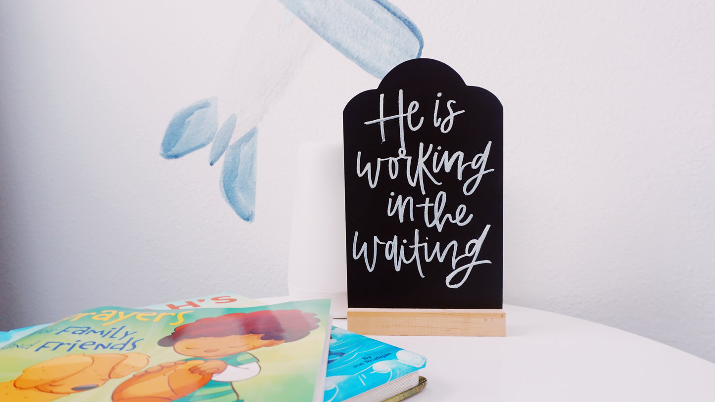 He Is Working in the Waiting - Tabletop Chalkboard Sign with Base - Light Color Wood